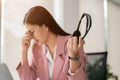 A stressed Asian female call centre agent holding a headset, sitting at her desk, feeling tired