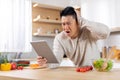 Stressed asian man cooking at home, reading food blog Royalty Free Stock Photo