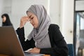 Stressed Asian Muslim businesswoman working at her office desk, suffering from a headache Royalty Free Stock Photo