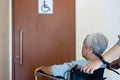 Stressed asian senior woman with wheelchair waiting on a long time at front disabled toilet,queue of disabled elderly waiting at