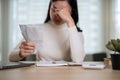 A stressed Asian woman is holding invoices or bills, calculating her monthly household expenses