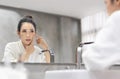 Stressed Asian woman in white Bathrobe looking at pimple on face into the mirror and try to squeeze it Royalty Free Stock Photo