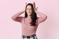 Stressed beautiful woman touching temples, lady having headache, keeps eyes closed while standing against pink wall, wearing rose