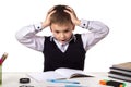 Stressed bewildered pupil sitting at the desk with hands over the head surrounded with stationery