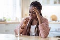 Stressed Black Lady Taking Painkiller Pill While Sitting At Table In Kitchen