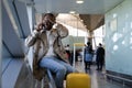 Stressed Black man in spectacles shocked with bad news, talking on mobile phone, sitting in airport, makes facepalm by hand and Royalty Free Stock Photo