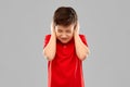 Stressed boy in red t-shirt closing ears by hands