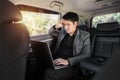 Stressed business man using laptop computer while sitting in the back seat of car Royalty Free Stock Photo