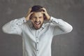 Portrait of a stressed angry young man screaming standing on a gray studio background Royalty Free Stock Photo