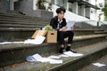 A stressed Asian businessman is reading his termination letter while sitting on the stairs