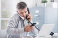 Stressed desperate businessman working in his office and having multiple calls, he is holding two handsets and a mobile phone,