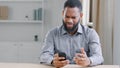 Stressed disappointed African American ethnic bearded man with mobile phone reading bad news. Office worker businessman