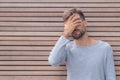 Stressed disappointed young guy making facepalm gesture with hand. Wooden wall background, copy space. Facepalm concept