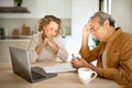 Stressed elderly couple checking financial papers, sitting with laptop and looking at loan documents, kitchen interior Royalty Free Stock Photo