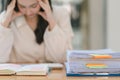 The stressed and exhausted millennial Asian businesswoman is seen sitting at her office desk with her hand on her head