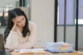 The stressed and exhausted millennial Asian businesswoman is seen sitting at her office desk with her hand on her head