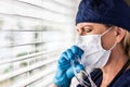 Stressed Female Doctor or Nurse Crying At Window Wearing Medical Face Mask and Goggles