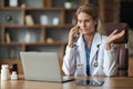 Stressed Female Doctor Talking On Cellphone And Using Laptop In Clinic Royalty Free Stock Photo