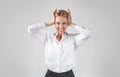 Stressed female office employee clenching her head, feeling angry or desperate on light grey studio background