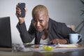 Stressed and frustrated afro American black woman working overwhelmed and upset at office laptop computer holding mobile phone in
