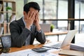 A stressed and frustrated Asian businessman is covering his face, sitting at his desk Royalty Free Stock Photo