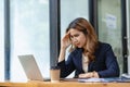 Stressed and frustrated asian female accountant sitting at desk making serious business decisions