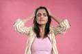 Stressed or having a headache businesswoman in suit holding her head with eyes shut isolated on pink background