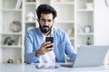 Stressed indian male freelancer looking at smartphone screen in home office Royalty Free Stock Photo