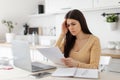 Stressed lady entrepreneur doing paperwork and working on laptop, sitting at table in kitchen, checking financial Royalty Free Stock Photo