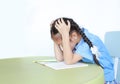 Stressed little girl in school uniform sitting at desk isolated over white background. Schoolgirl unhappy doing homework. Student