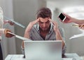 Stressed man on laptop desk surrounded by files phones tablets in office