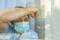 Stressed man in protective mask looking out of window, view through glass. Self-isolation during COVID-19 pandemic Royalty Free Stock Photo