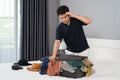 Stressed man trying to close overfilled suitcase on bed Royalty Free Stock Photo