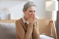 Stressed middle aged woman sit on sofa in living room, lost in thought
