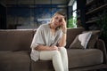 Stressed middle aged woman sit on sofa in living room, lost in thought