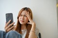 Stressed millennial Asian female using smartphone, suffering from headache or migraine