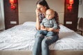 Stressed mother with little child sitting on bed