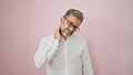 Stressed out young hispanic man, grey-haired and handsome, battling crippling cervical back ache over isolated pink background