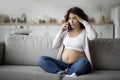 Stressed Pregnant Woman Talking On Cellphone While Sitting On Couch At Home,