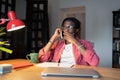 Stressed puzzled African American man freelancer making phone call sits at table with laptop and mug