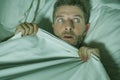 Stressed and scared man alone in bed awake at night in fear after having a nightmare feeling paranoid holding the blanket in
