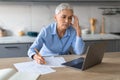 Stressed senior lady working on laptop taking notes touching head Royalty Free Stock Photo