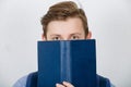 Stressed student covering half face with a opened blue book. Difficult task concept, discontent guy looks lost, dissatisfied