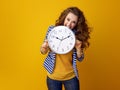 Stressed stylish woman against yellow background biting clock