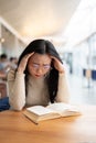 A stressed and tired Asian female college student is reading a book in a library. Royalty Free Stock Photo