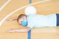 Stressed tired exhausted child with blue mask and  ball in a physical education lesson. Safe back to school during pandemic concep Royalty Free Stock Photo