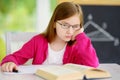 Stressed and tired schoolgirl studying with a pile of books on her desk Royalty Free Stock Photo