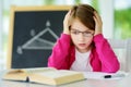 Stressed schoolgirl studying with a pile of books on her desk. Young girl doing her homework. Education and distance learning for