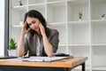 Stressed and unhappy Asian businesswoman sits at her desk suffering from headache Royalty Free Stock Photo