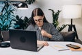 Stressed upset young female in eyeglasses having heart attack sitting on couch at home office. Worker fatigued from computer at